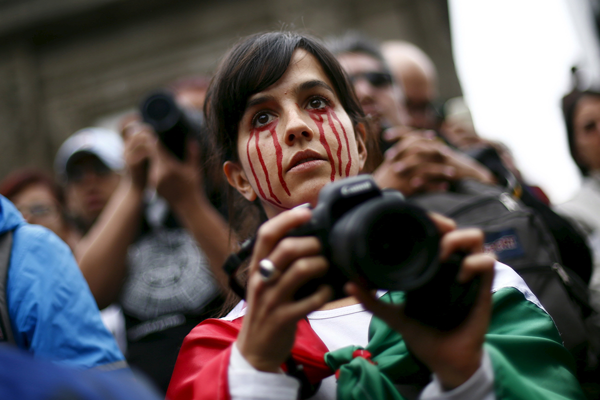 A woman with red paint on her face takes photos during a march 