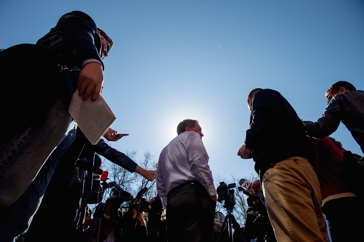 John Kasich, seen from behind, speaks to reporters outdoors while campaigning in Columbia, South Carolina