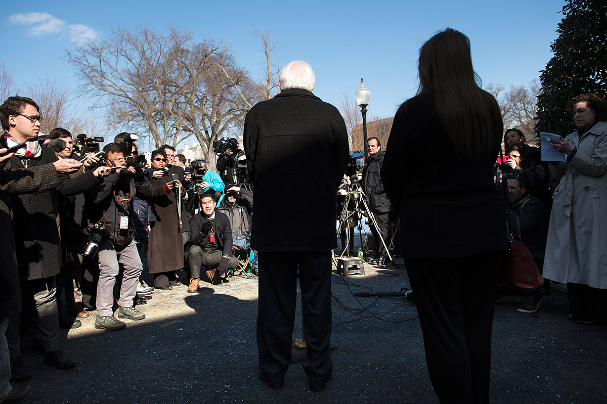 Bernie Sanders, seen from behind, stands outside the White House speaking to reporters after meeting with President Obama