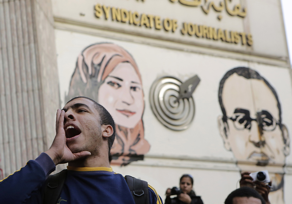 An Egyptian chants slogans denouncing toppled President Hosni Mubarak during a protest in front of the press syndicate in Cairo, Egypt, Tuesday, Dec. 2, 2014. A judge on Saturday dismissed the case against Mubarak and acquitted his security chief over the killing of hundreds of protesters during Egypt’s 2011 uprising. Graffiti on the wall shows Al-Housseiny Abu Daif, right, and Mayada Ashraf, left, two journalists who were shot to death during separate clashes following the 2011 popular uprising. (AP Photo/Amr Nabil)