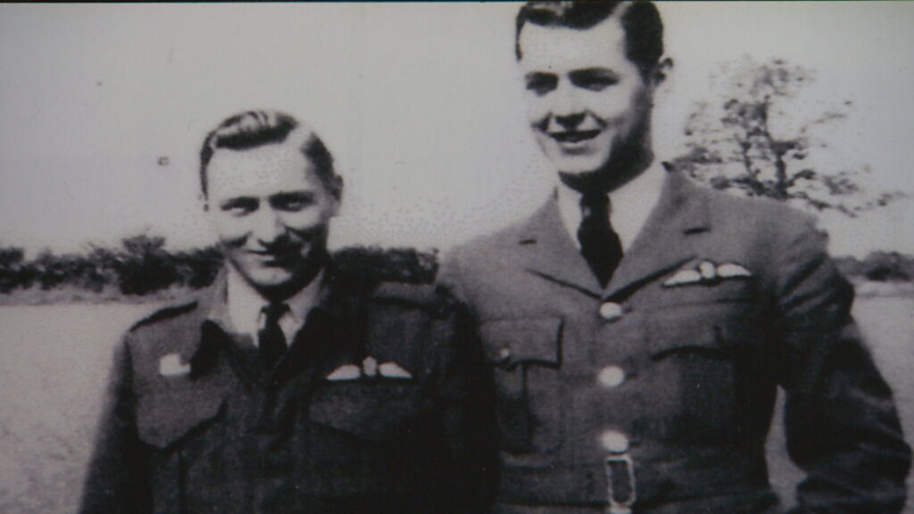 black and white picture of two men dressed in Canadian military uniforms, smiling at the camera. one man is taller than the other with darker hair, the other is blonde and is a bit shorter.