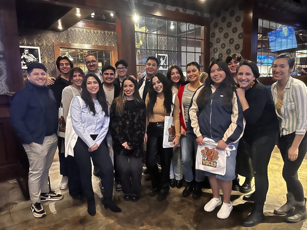 a group 15 or so journalists gather together in a crowd to take a group photo in a restaurant