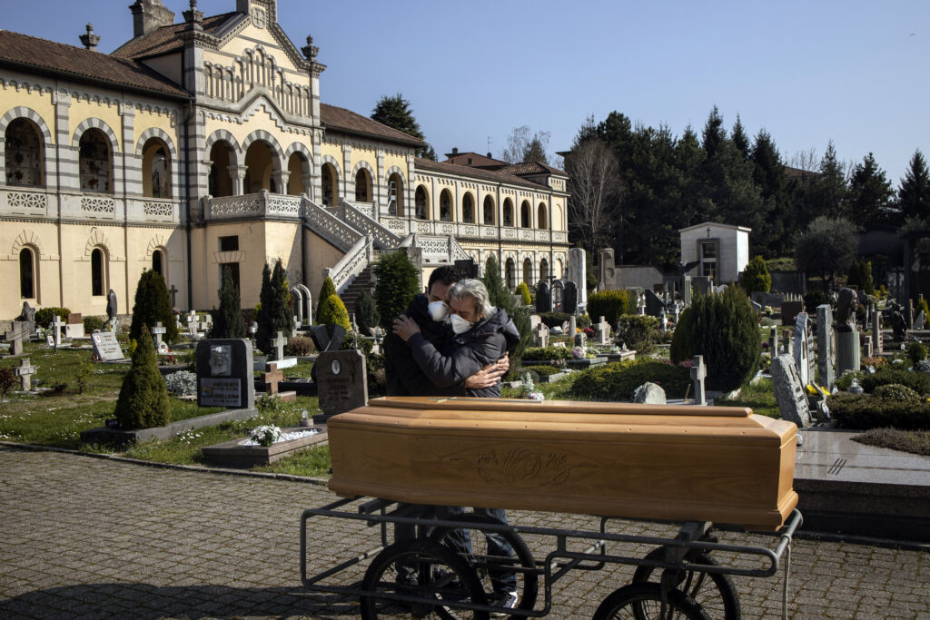 two people embracing outside of a church in Italy next to a coffin