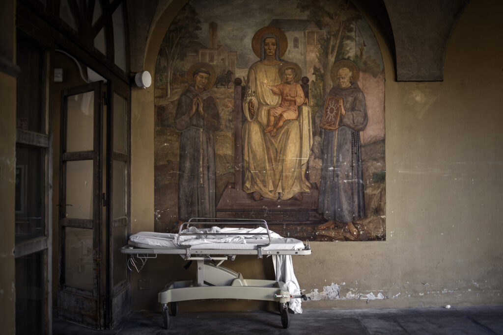 a stretcher outside of a courtyard, there is an Italian religious fresco on the wall in the background