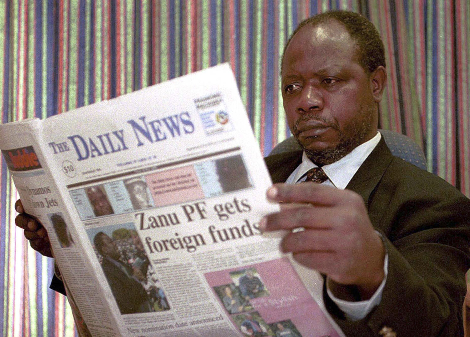 picture of geoffrey nyarota, wearing a black suit and tie, reading the daily news, a paper he famously founded for accountability journalism