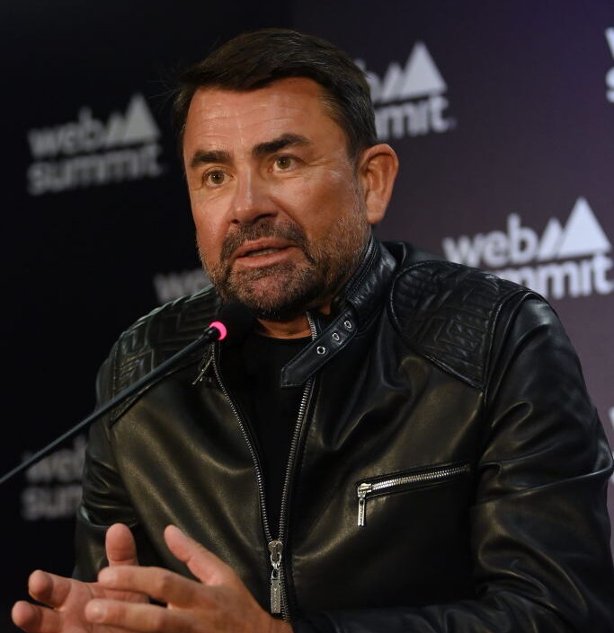 man in all black clothes speaks at a panel with a microphone