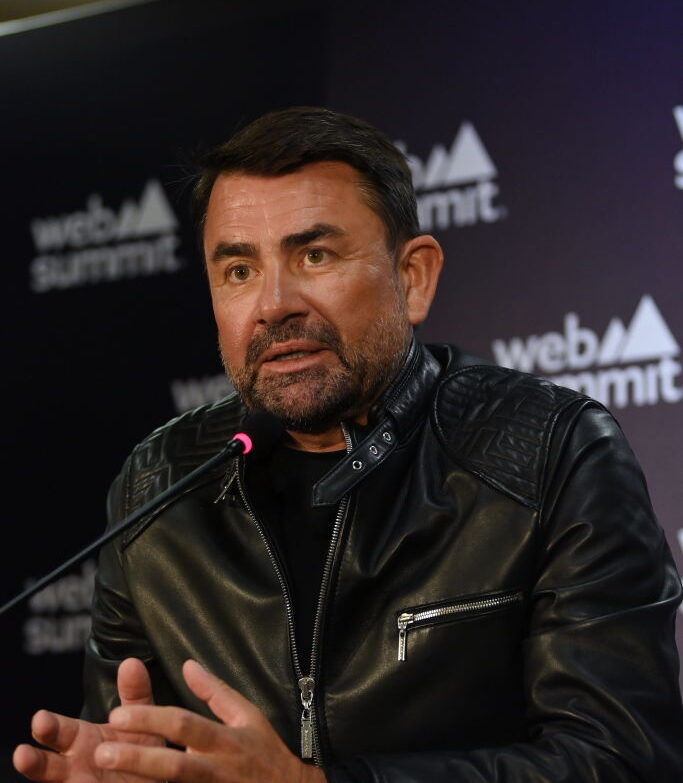 man in all black clothes speaks at a panel with a microphone