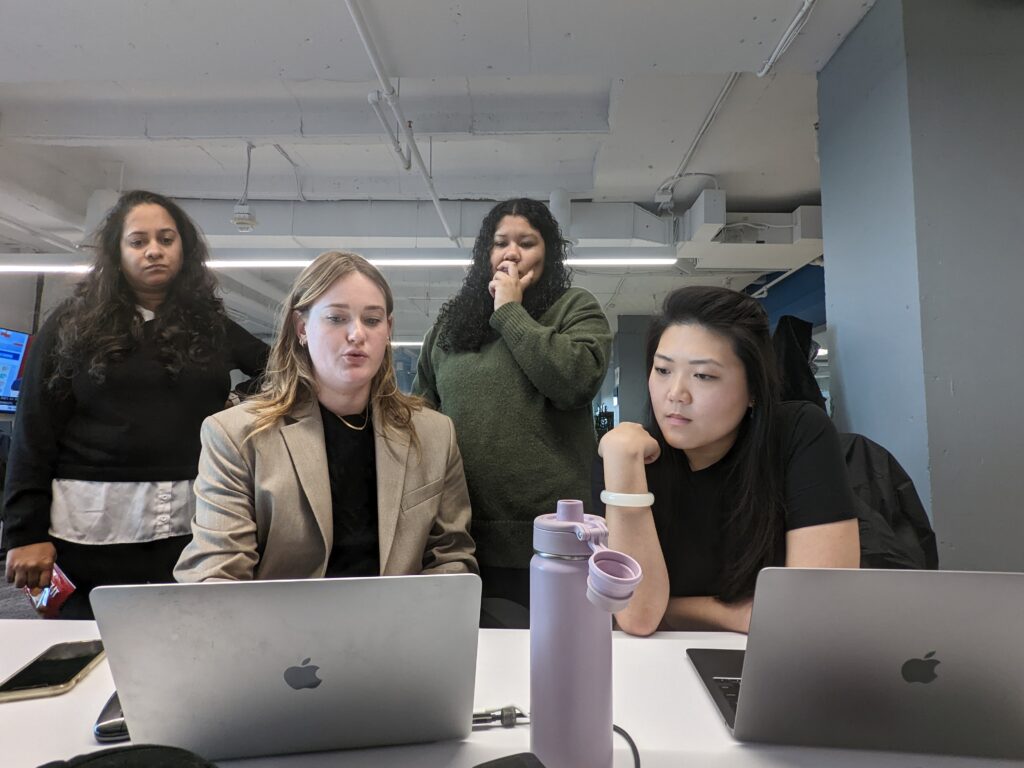 four people sit together in front of a laptop inside a newsroom