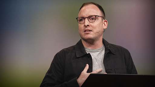 Isaac Saul wearing glasses, a gray shirt, and black button down, during his Ted talk