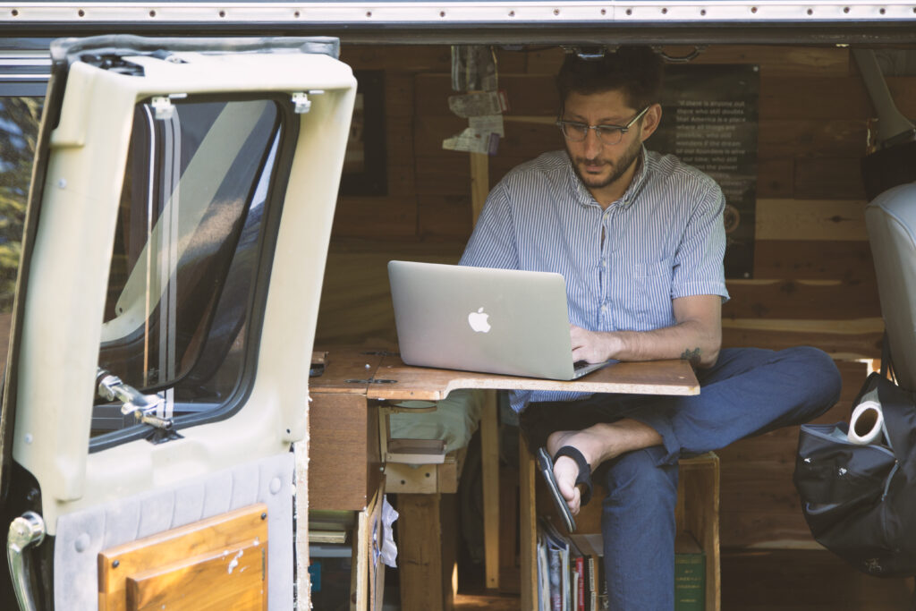 dan sits in a van while working at a makeshift desk