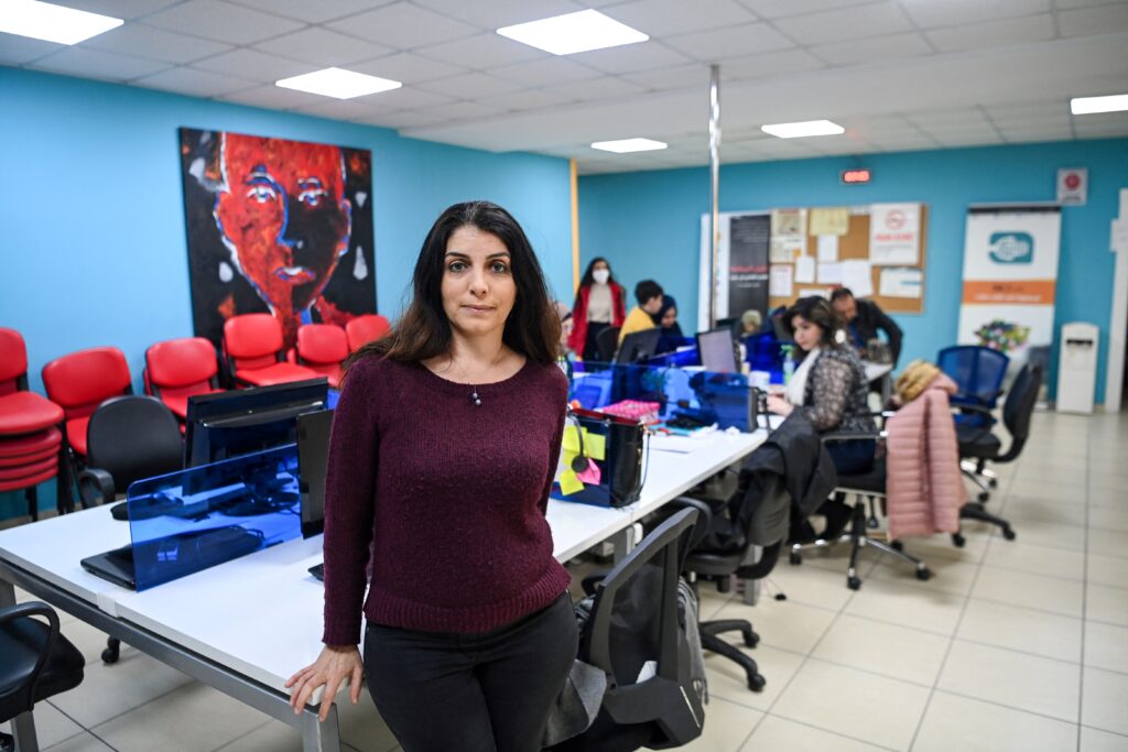 lina chawaf sits on the edge of a table in her newsroom