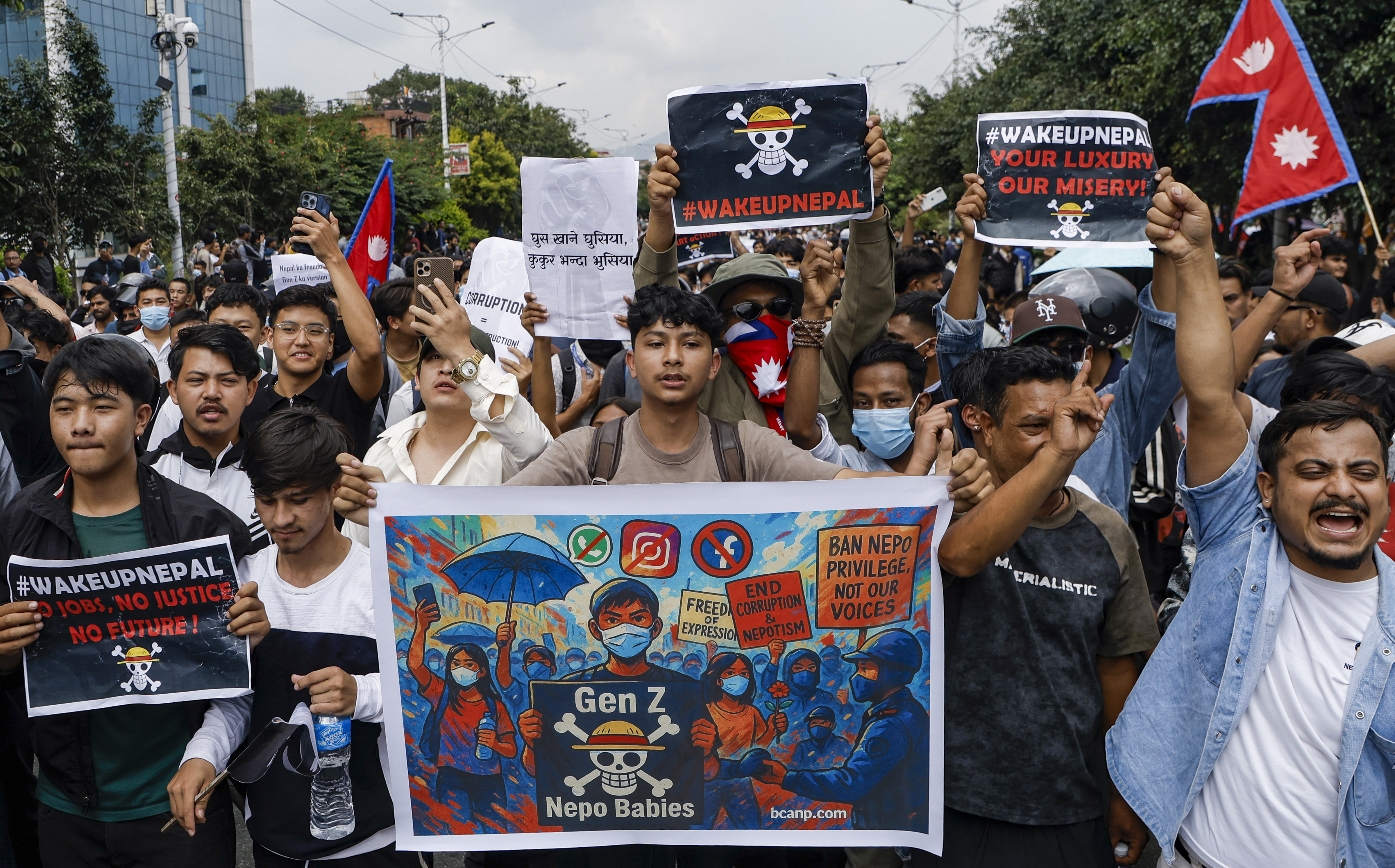 students march in protest, holding banners with anti-corruption slogans and the one piece skull and crossbones logo