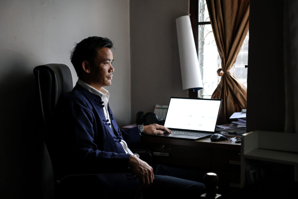 man sits in a dark office, the curtains to his window are only open a sliver