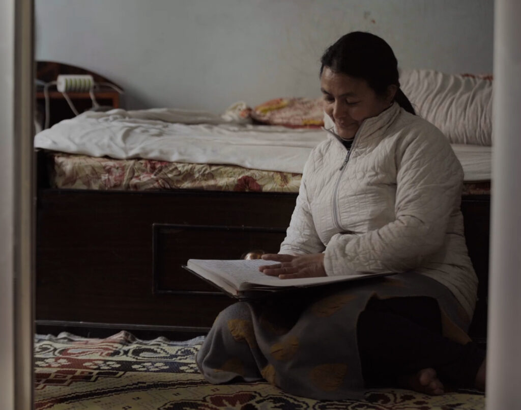 Devi in her bedroom, sitting cross legged on the floor, reading her diary