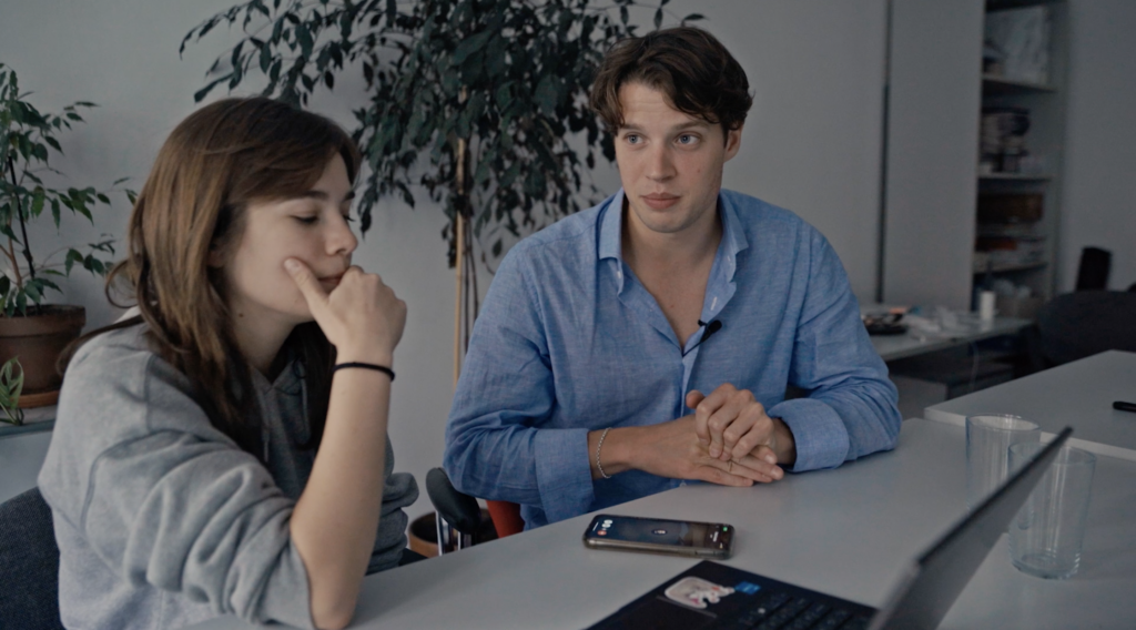two reporters sit side by side at a table