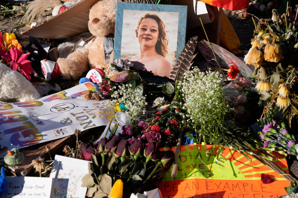 flowers, teddy bears, and a framed portrait of renee good at her memorial site