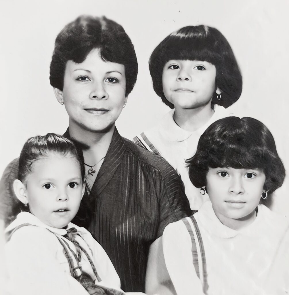 a black-and-white family photo with Marcela, her two sisters, and mother. The children in the photo are young, below the age of ten.