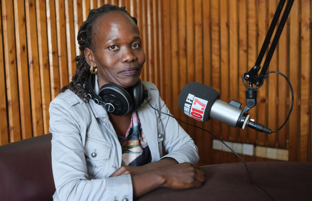 a woman sits at a radio mic stand in a recording studio