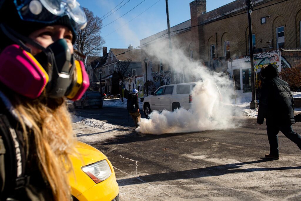 People react to copious tear gas and flash grenades deployed by federal agents near the scene of 26th Street and Nicollet Avenue