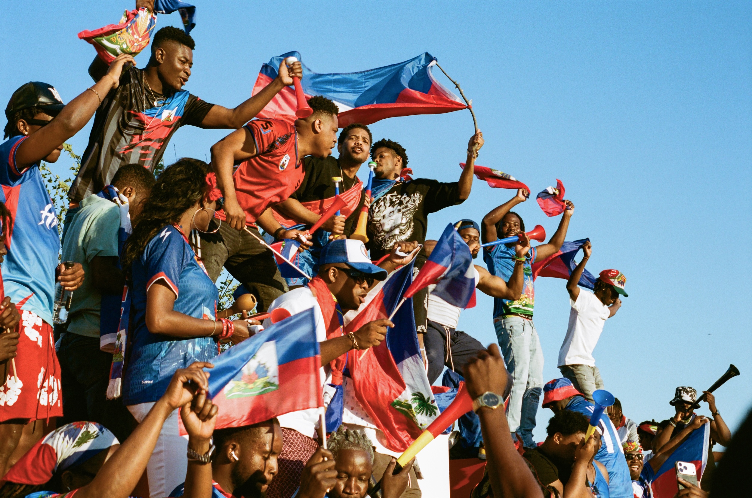 haiti fans wave flags and stand on top of a sign in Philly outside the stadium