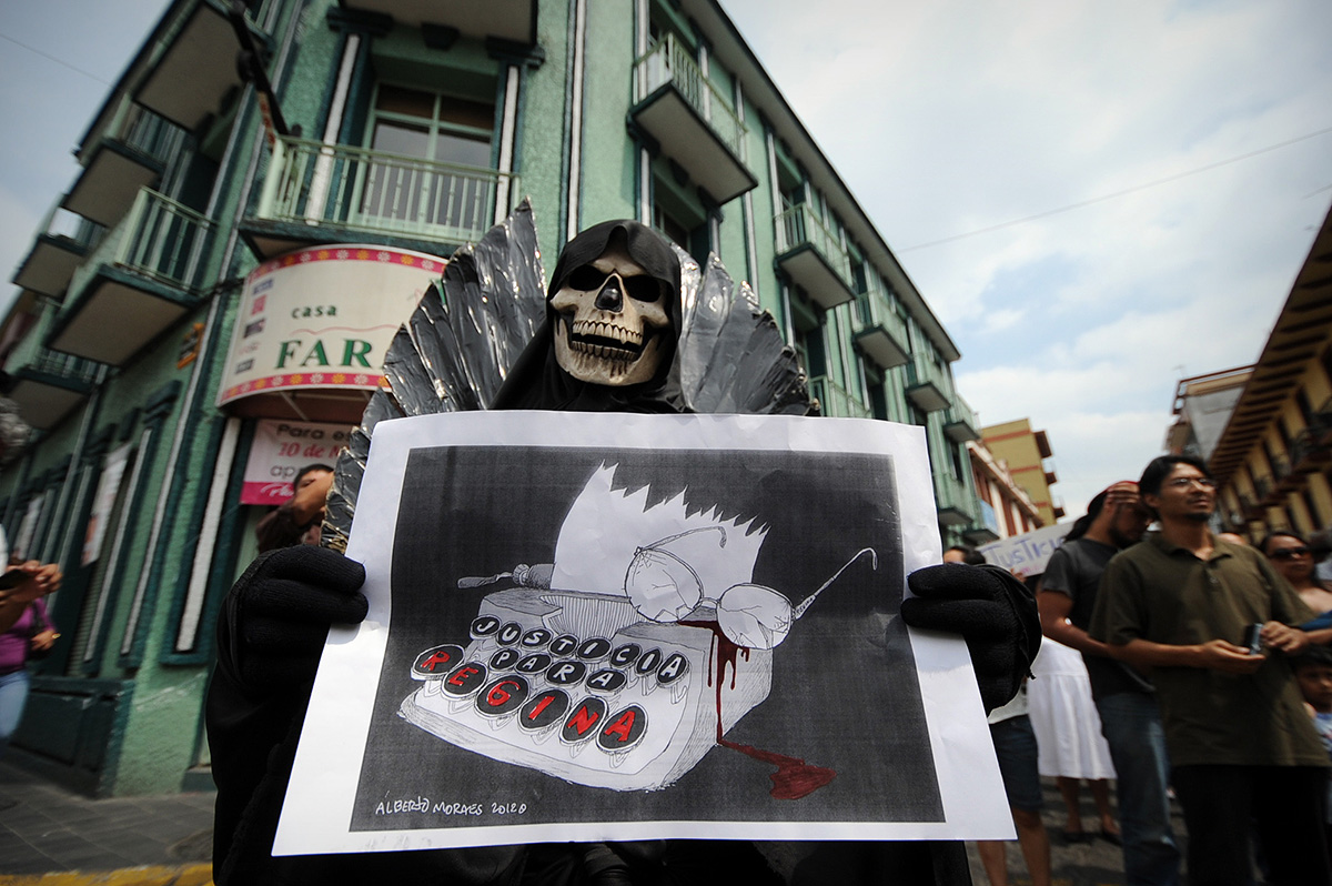 Protestor in a skeleton mask holds a sign reading "justice for Regina"