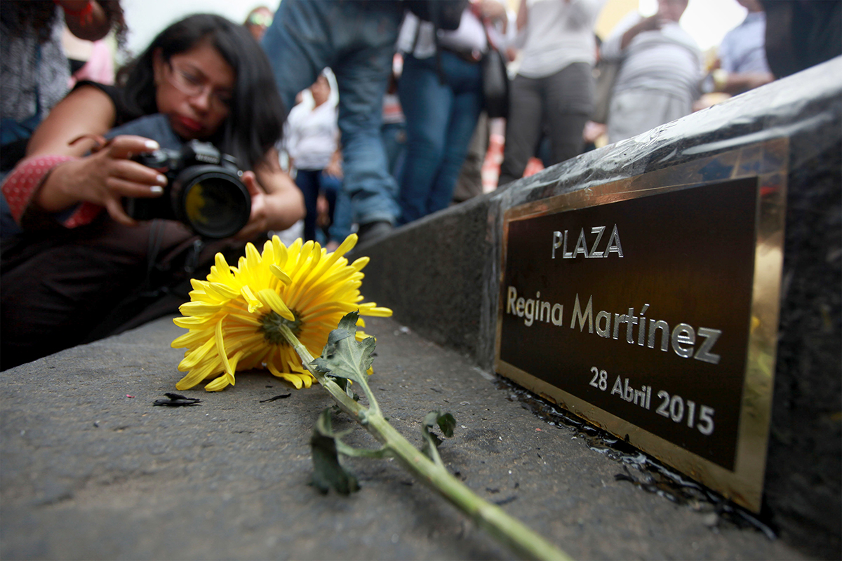 A woman takes a photograph of a plaque reading "Plaza Regina Martínez. April 28 2015"