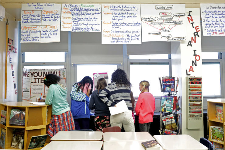 Students in a 6th grade News Literacy class examine an assignment given by their teacher, Marisol Solano (center,) at the Herbert S. Eisenberg I.S. 303 school in Brooklyn