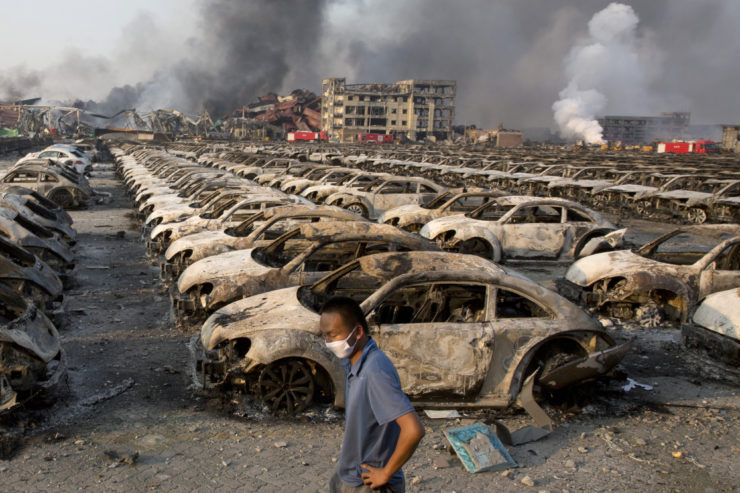 A man walks past the charred remains of new cars at a parking lot near the site of an explosion at a warehouse in northeastern China's Tianjin municipality. Satellite imagery helped reporters navigate the site