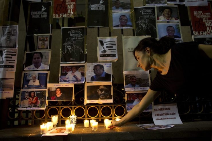 A woman lays a candle in front of pictures of murdered journalists taped to a fence in Mexico City the day after Javier Valdez was killed