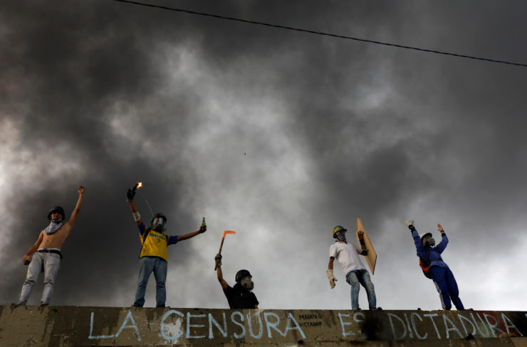 Demonstrators gesture to riot security forces while rallying against President Nicolás Maduro over graffiti that reads "censorship is dictatorship" in Caracas, Venezuela, May 2017