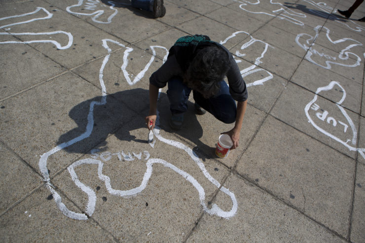 A woman paints the name of a victim of the Mexican drug war onto a body outline as part of a memorial for those killed at the Monument for the Mexican Revolution in Mexico City in December 2016, the 10th anniversary of the drug war's start
