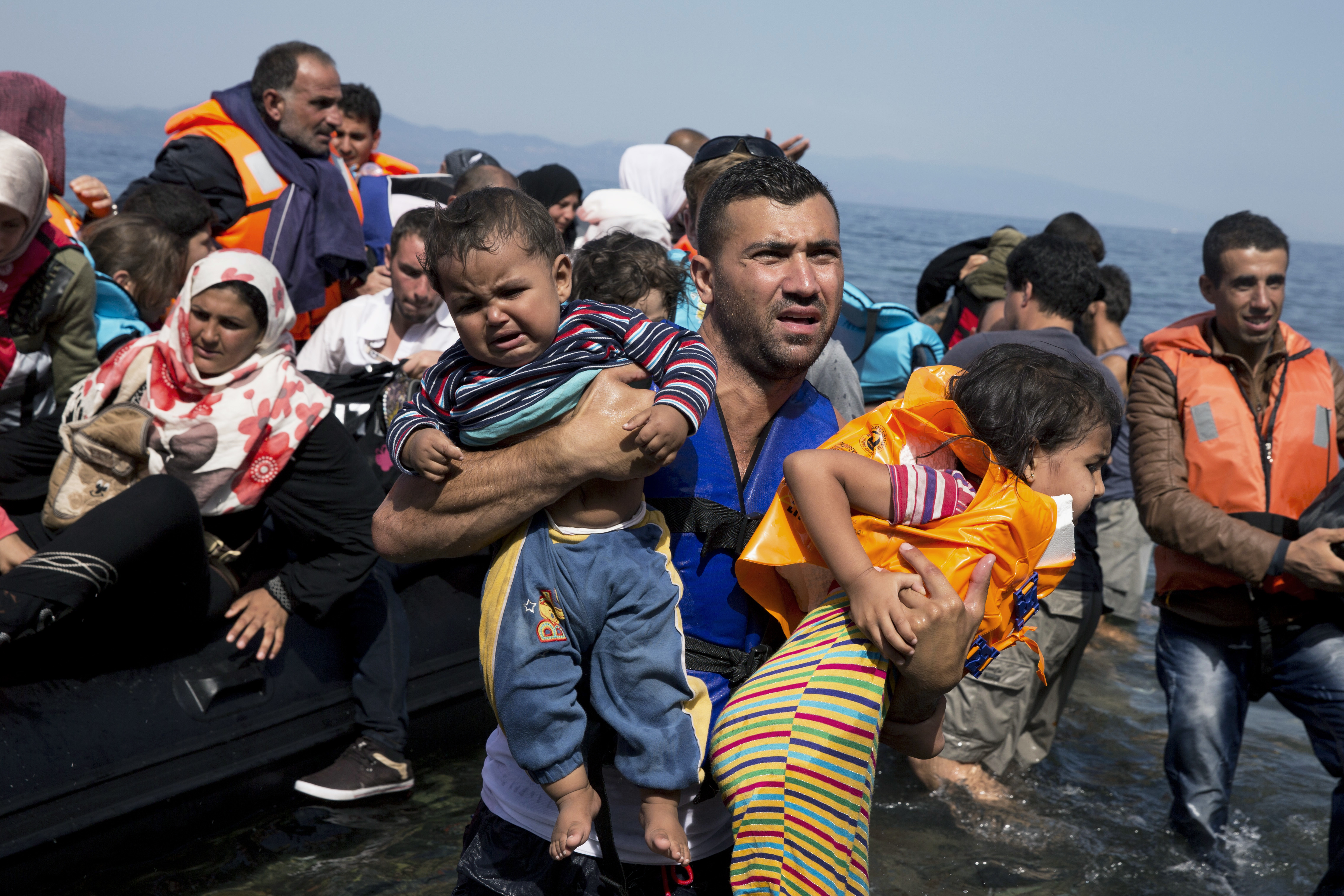 An aid worker carries two young children as Syrian refugees arrive on an overcrowded dinghy after crossing from Turkey to the island of Lesbos, Greece in 2015. The social upheaval related to the influx of refugees into Europe led a group of Greeks and migrants from several countries to launch Solomon