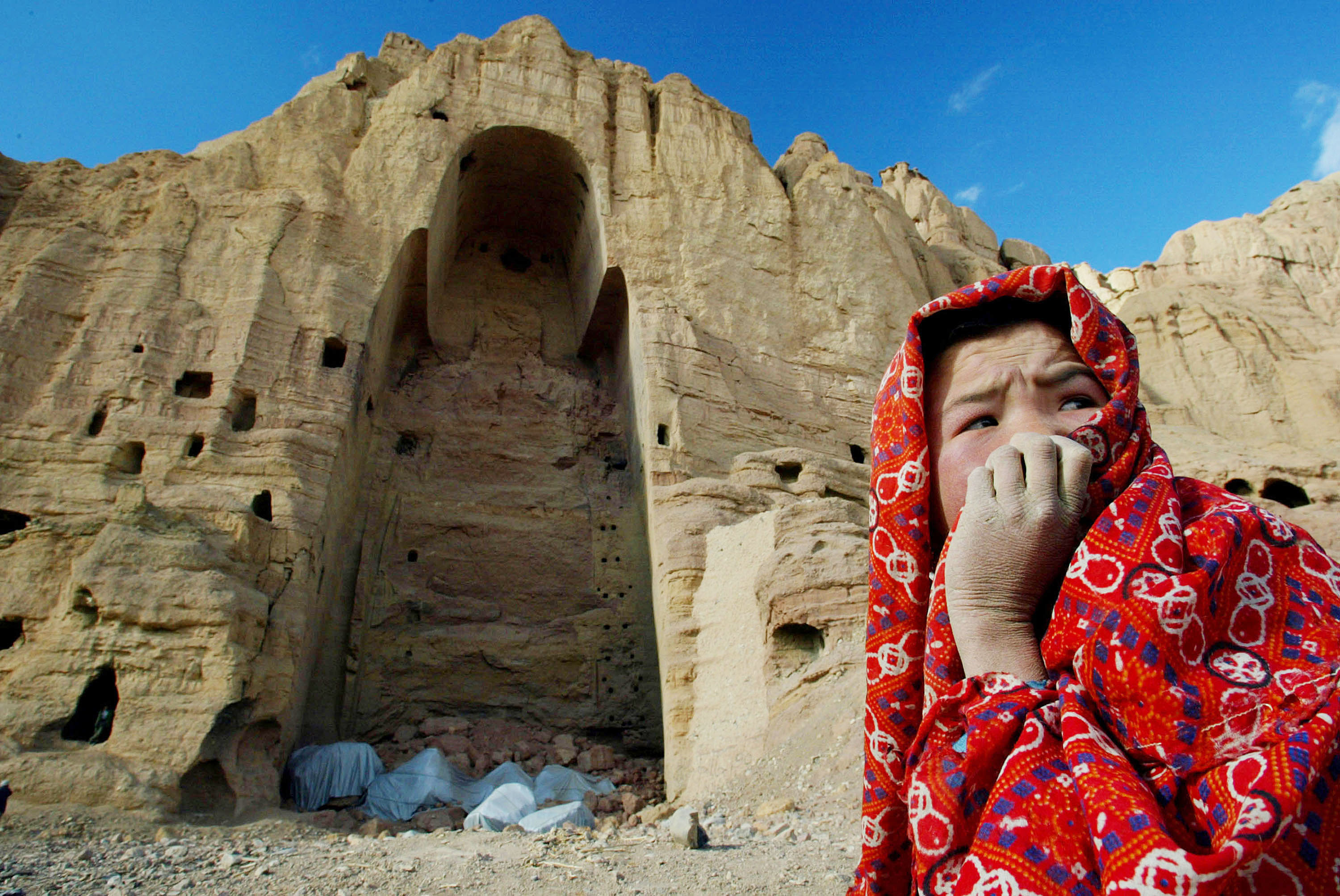 A local Afghan girl sits in front of the site of a 2001 Taliban explosion