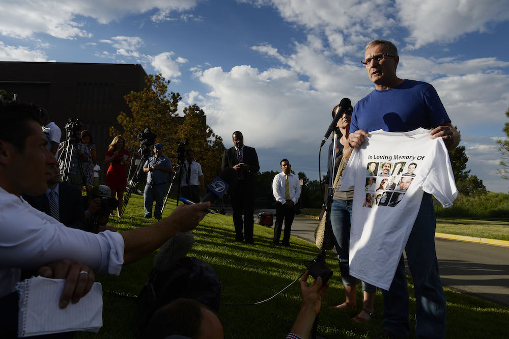 Tom Teves holds up a T-shirt with photos of all 12 victims of the 2012 Aurora movie theater shooting, including his son, Alex Teves, at a press conference in Centennial, Colorado in 2015. Teves is an advocate of “strategic silence,” and founded the organization No Notoriety to push for starving mass shooters of media attention