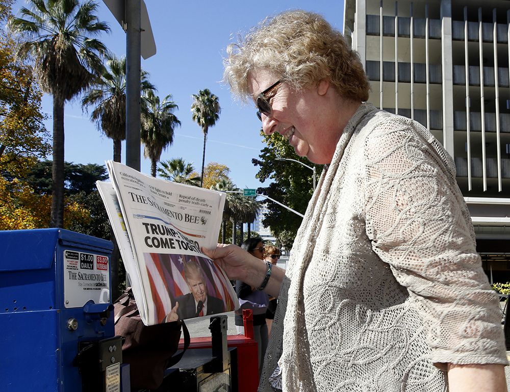 A woman looks over the front page of the Sacramento Bee she purchased from a vending machine in Sacramento the day following the 2016 presidential election