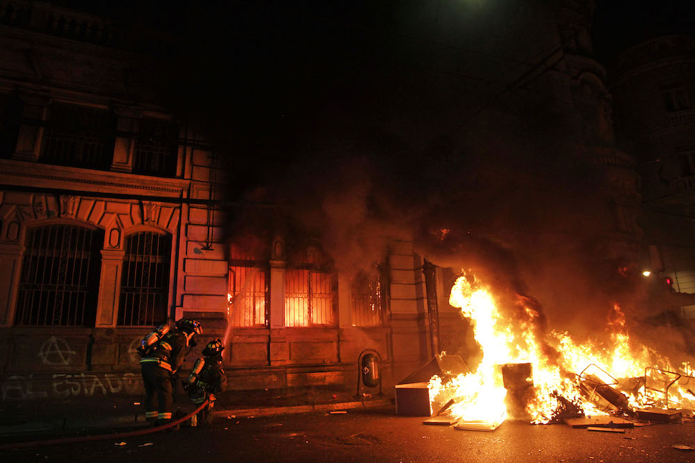 Set amidst a series of violent protests, a fire engulfs the front of the building of El Mercurio newspaper in Valparaíso, Chile in October 2019.