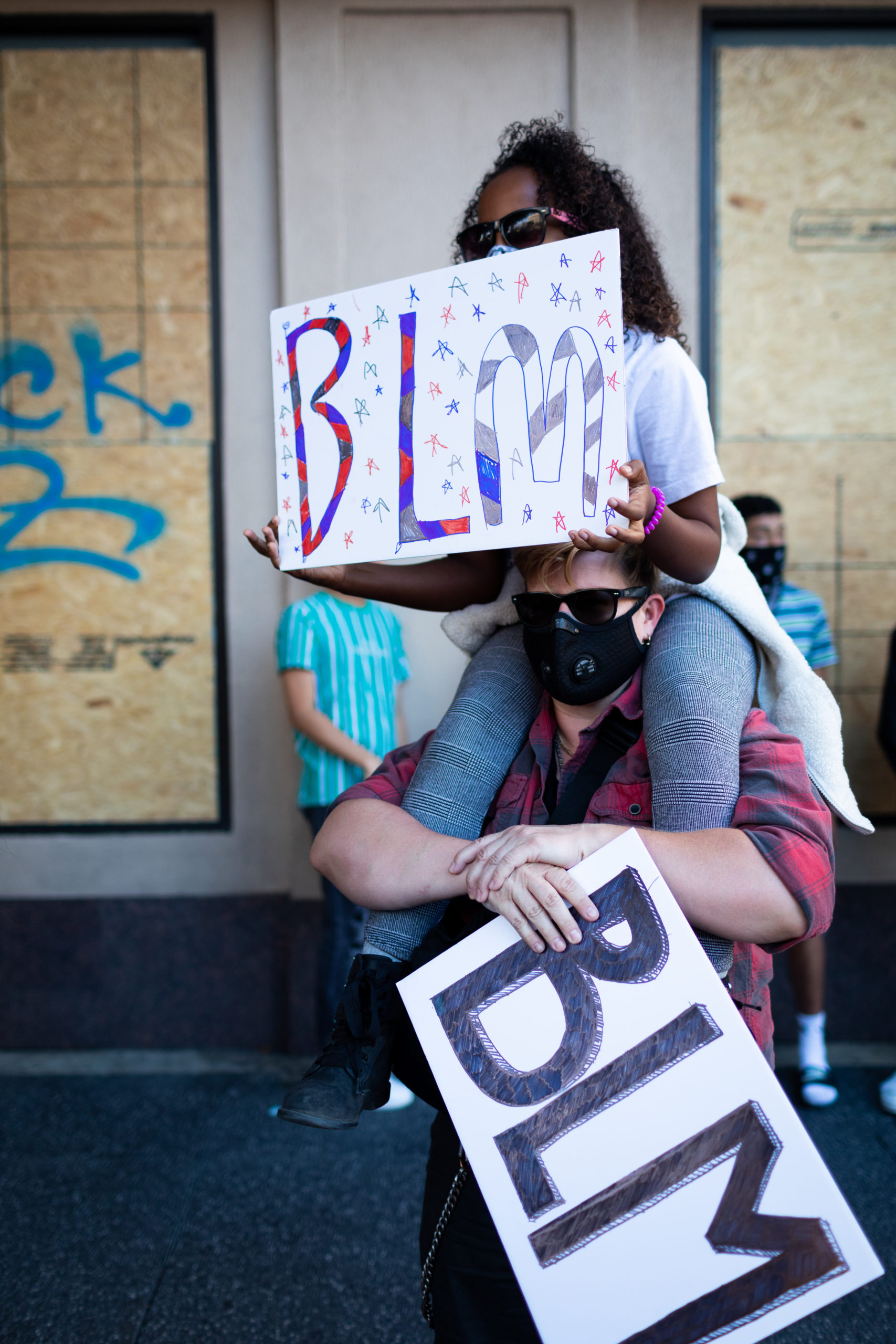 Young girl sits on top of her step-mother's shoulders with a sign supporting Black Lives Matter