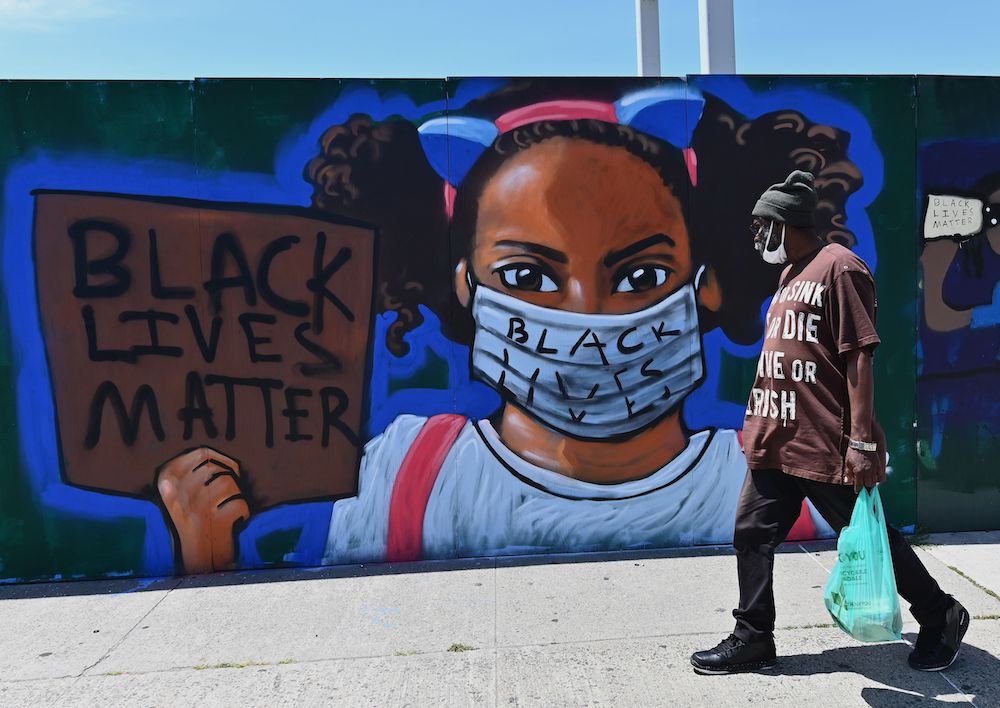 A person walks past a street mural of a girl holding a Black lives matter sign