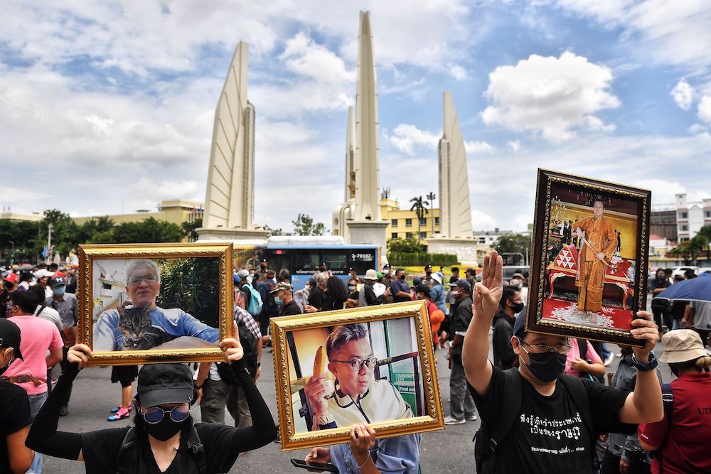 Anti-government protesters hold photos of self-exiled Thai academics Somsak Jeamteerasakul (right), Pavin Chachavalpongpun (center), and ex-Reuters journalist Andrew MacGregor Marshall — all threatened under Thailand’s strict lèse-majesté laws — at a rally by Democracy Monument in Bangkok in August 2020