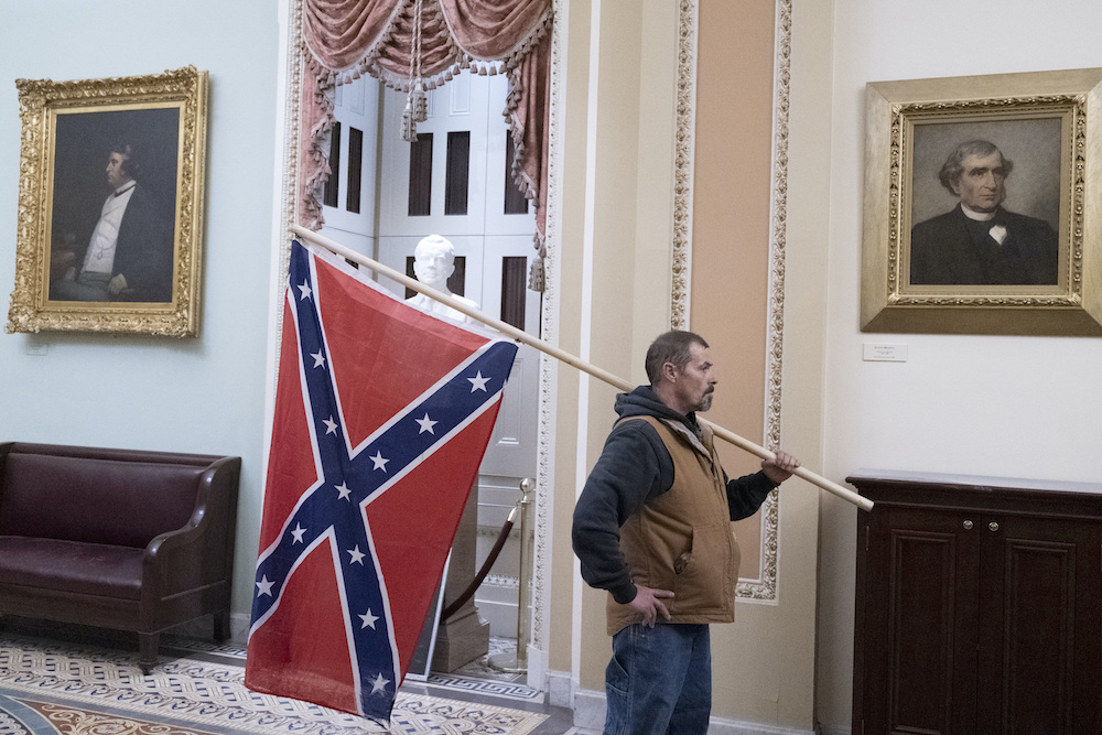 Trump loyalist roams halls of Capitol waving Confederate flag.