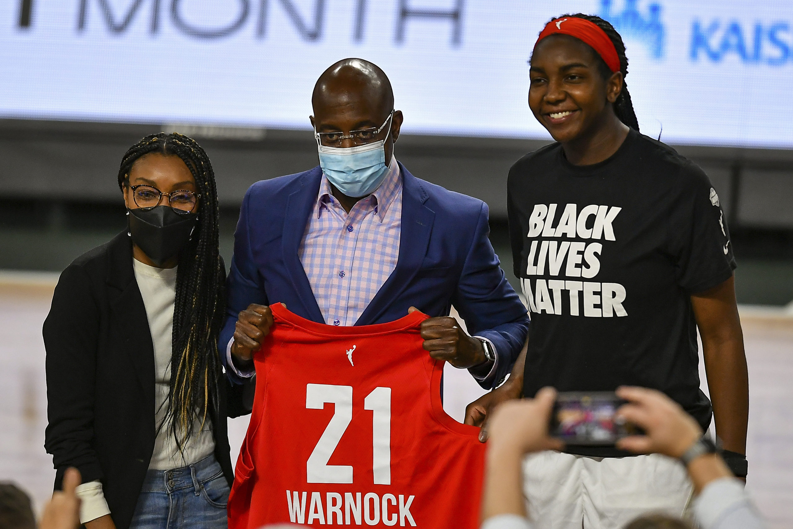 US Senator Raphael Warnock receives a jersey from Atlanta's Elizabeth Williams (1) at halftime during the WNBA game between the Phoenix Mercury and the Atlanta Dream on Aug. 21, 2021 at Gateway Center Arena in College Park, GA