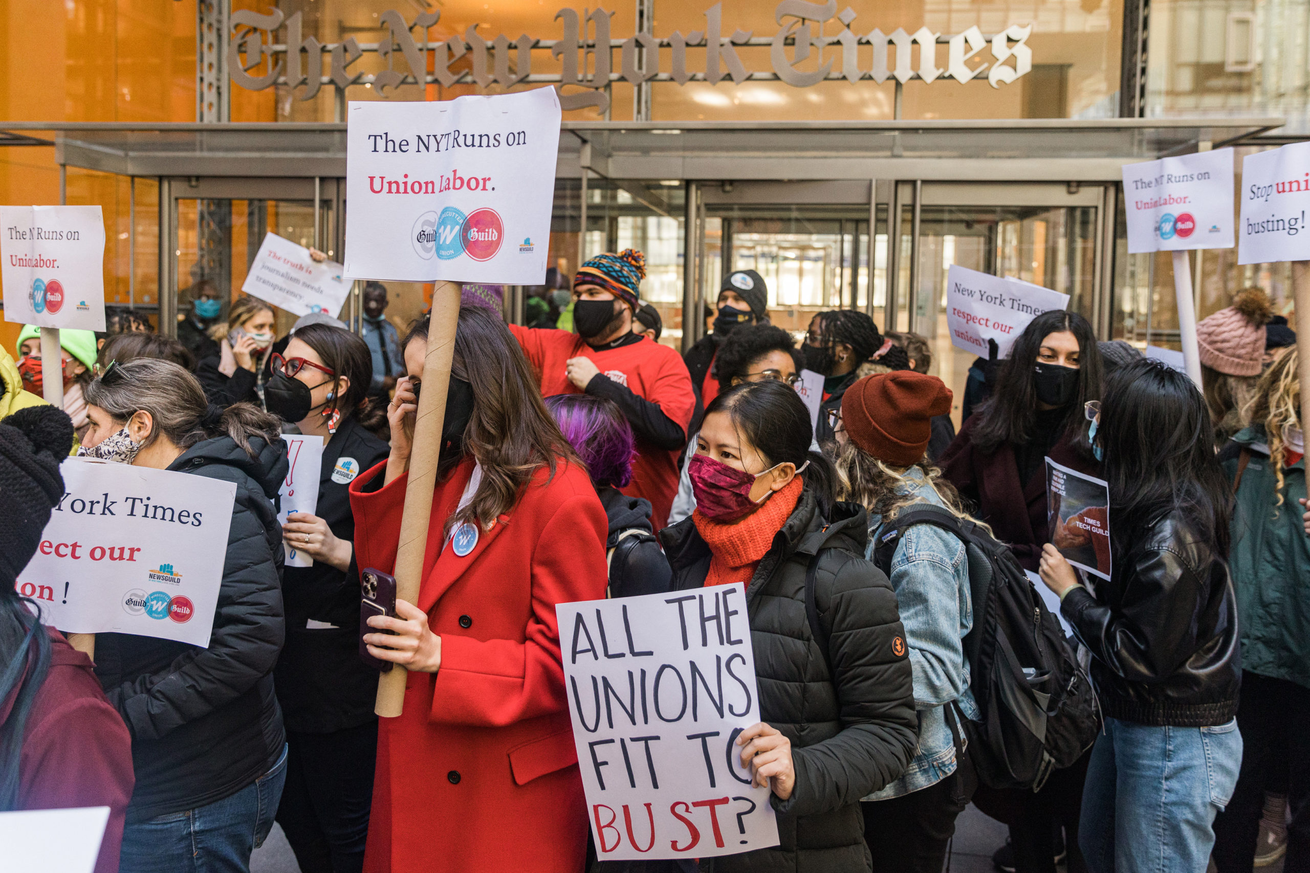 A crowd of Wirecutter employees protest outside the headquarters of The New York Times. One union member holds a sign that reads, "All the unions fits to bust?"