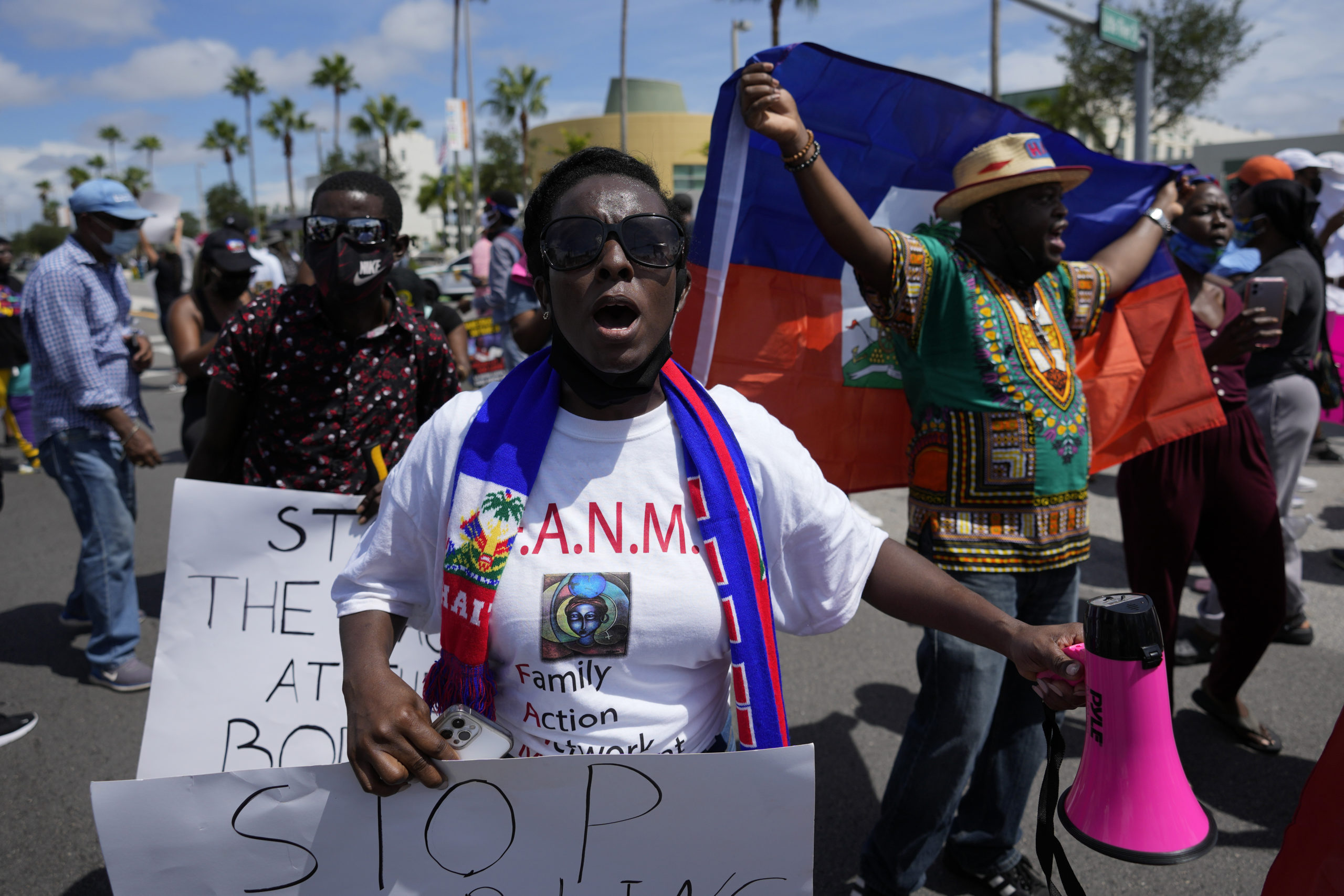 A woman holds a sign as she leads a group of protesters . Protesters behind her hold up Haitian flags.