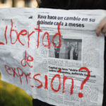 A protester holds up a newspaper spread that reads, in red paint, "¿Libertad de expresión?" (In English: Freedom of expression?)