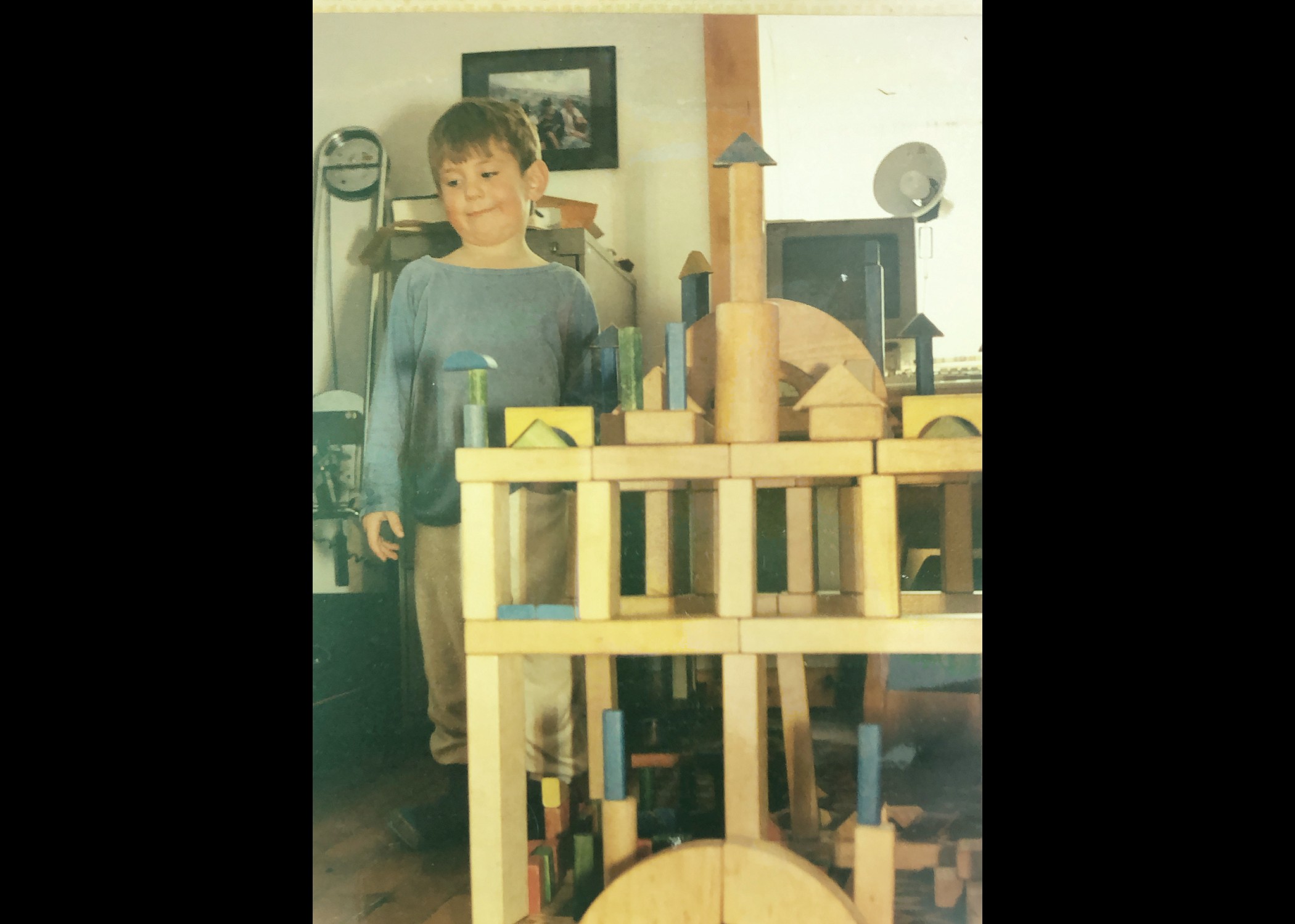 Reueben Fischer-Baum as a toddler stands next to one of his wooden block building creations