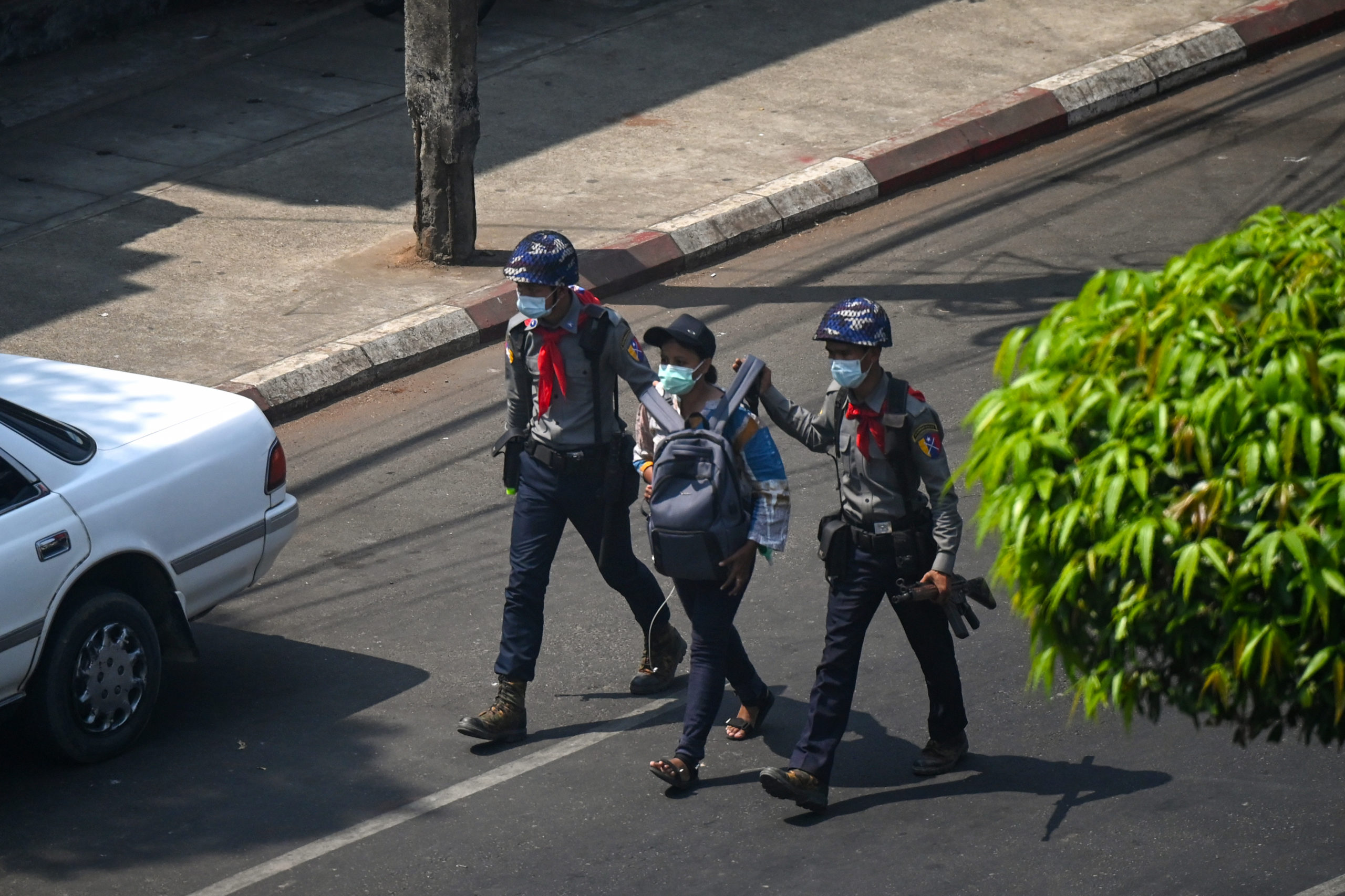 Kay Zon Nwe wears a backpack on her front as two police officers walk on either side of her, grabbing the arms of the backpack, as they walk down the middle of a road