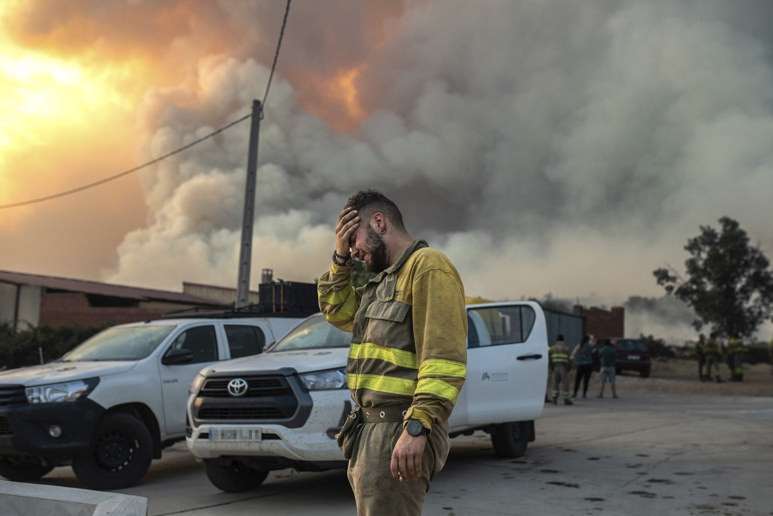 In the foreground is a large cloud of smoke, with a glimpse of flame behind it. At the center, a firefighter stands with his head in his hand.