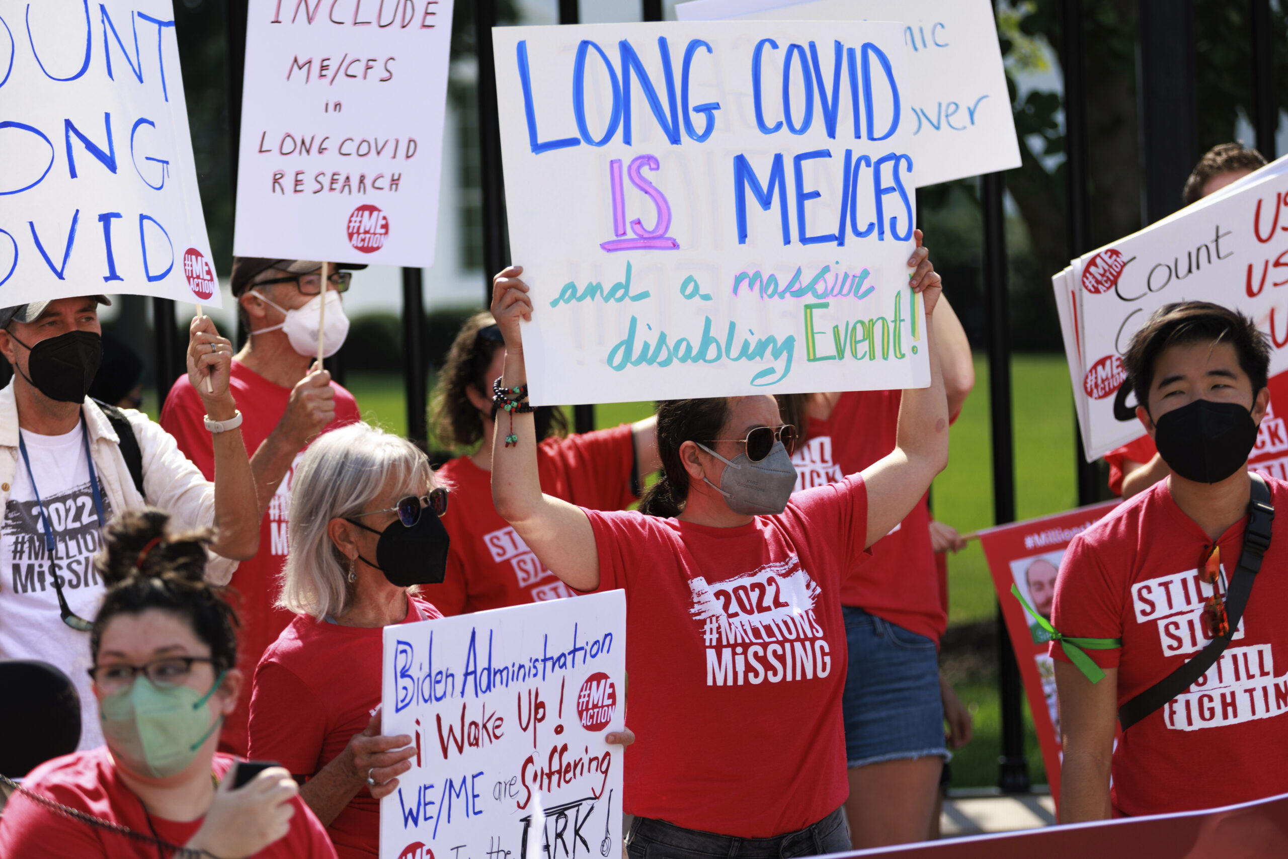 dozens of demonstrators donning red t-shirts hold protest signs saying LONG COVID IS ME/CFS and COUNT LONG COVID outside the White House gates
