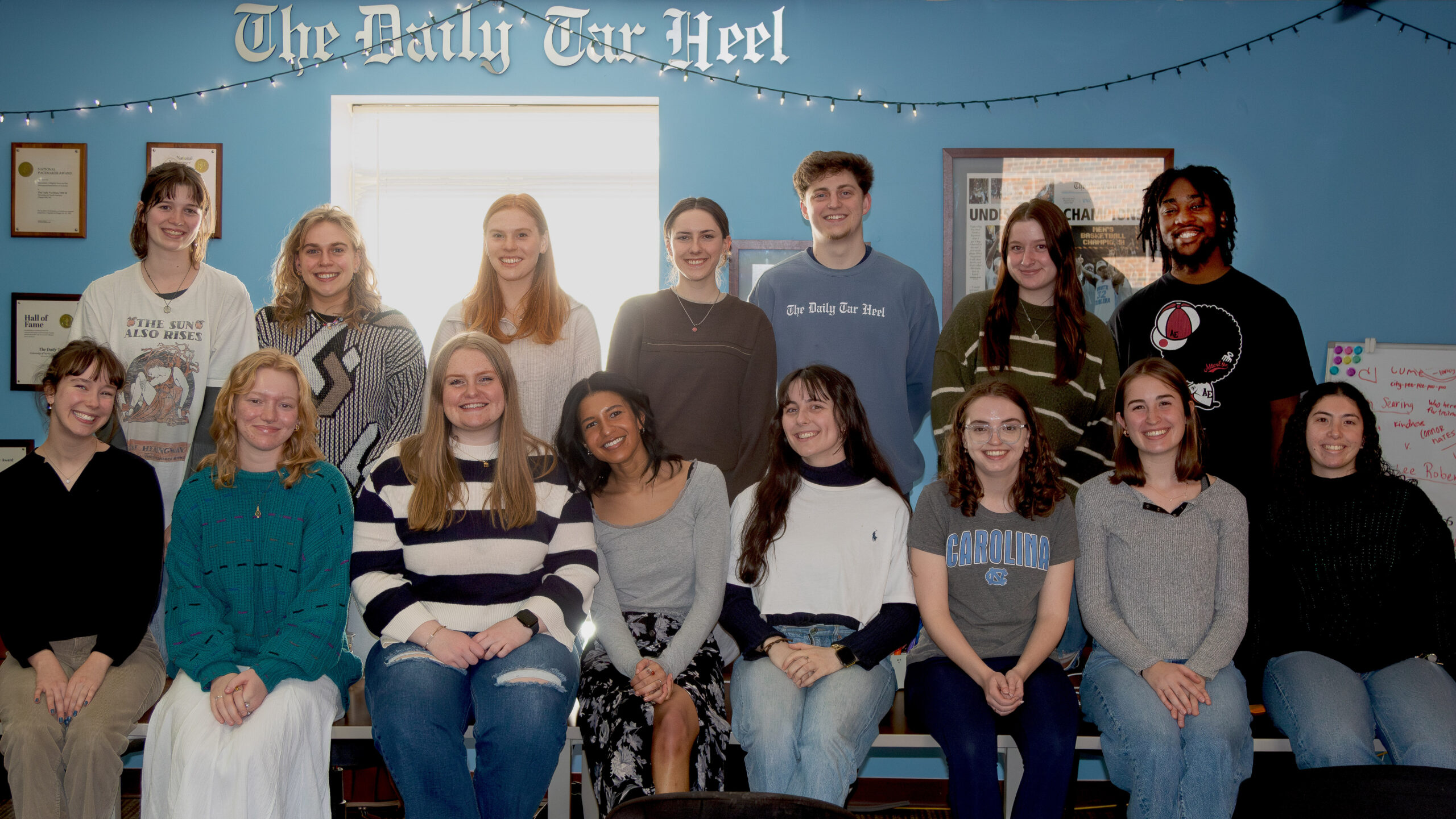a group of the Daily Tarheel's newsroom is posed together for a group picture. the wall is painted UNC Chapel Hill's baby blue school color.