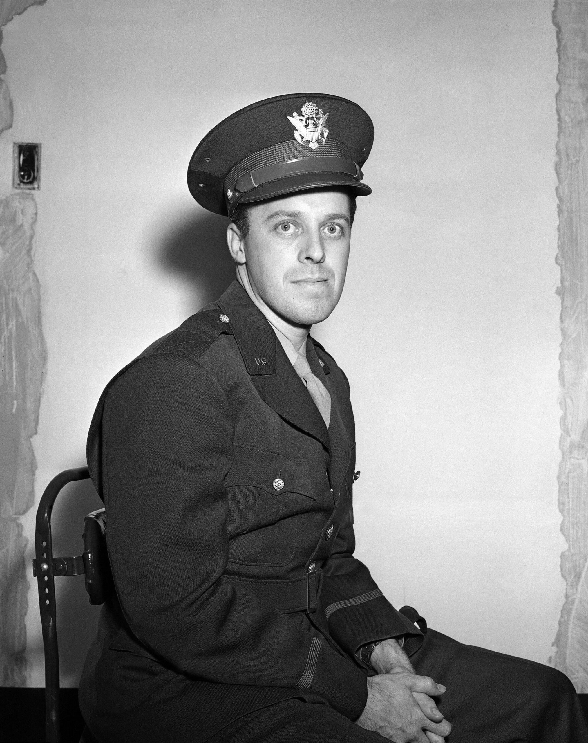 a black and white photograph of a journalist sitting for a portrait, wearing a U.S. military uniform